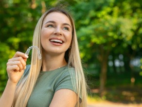 A smiling, confident woman holding an aligner in an outdoor setting