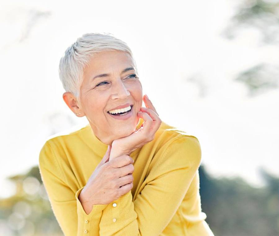 Older woman in yellow sweater smiling as she enjoys time outdoors