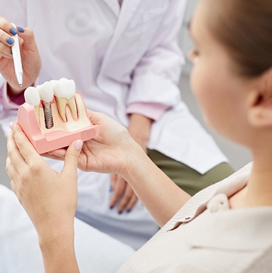 A dentist explaining dental implant parts with a tooth model